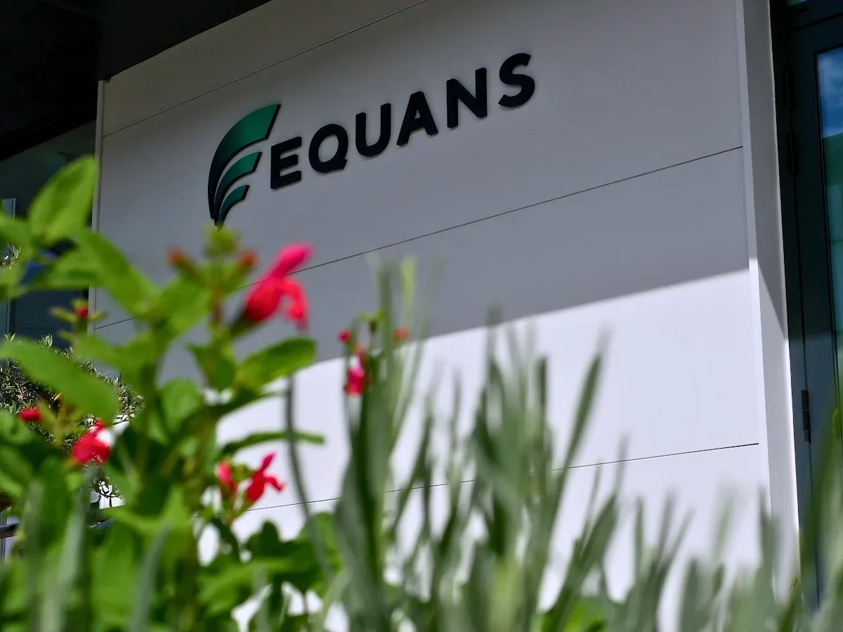 Enseigne Equans sur la façade des locaux, derrière des plantes en fleurs